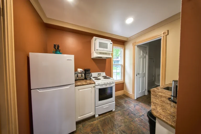 Small kitchen with a white refrigerator, white stove, and microwave mounted above; coffee maker and toaster on the counter, brown walls, and a window beside the stove.
