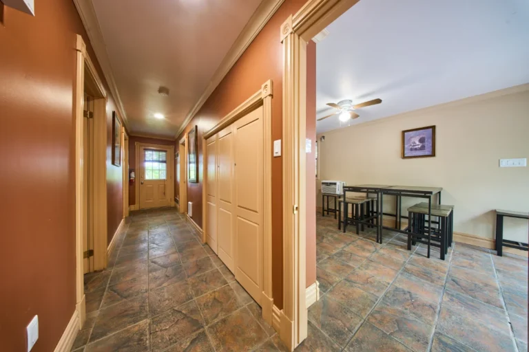 Long hallway with brown walls and tiled floor, doors along the hall, ending at a door with a window.