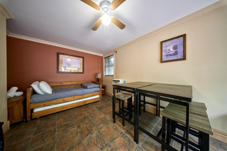 Cozy room with a wooden daybed on a red accent wall, gray bedding and pillows, plus a small side table and lamp.